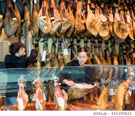 Young female and male vendors arranging jamon at counter in butcher shop Young female and male vendors arranging jamon at counter in butcher shop 141193622