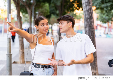 Positive tourist couple walking around foreign city on summer day, pointing at sights 141193667