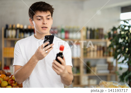 In shop young man scans QR code and take reading on soy sauce package using phone camera 141193717