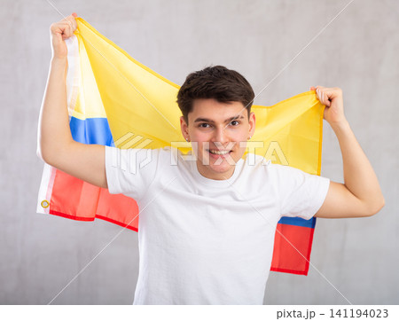Happy young man holding flag of Colombia against unicoloured background Happy young man holding flag of Colombia against unicoloured background 141194023