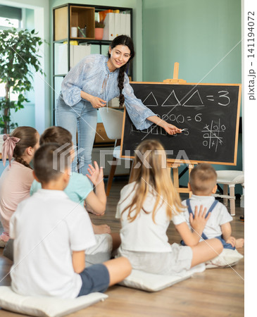 Teacher draws on blackboard and explains arithmetic and literacy lessons to children in kindergarten Teacher draws on blackboard and explains arithmetic and literacy lessons to children in kindergarten 141194072