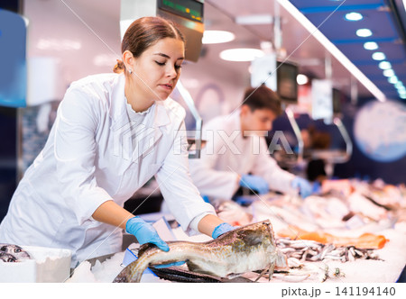 Positive saleswoman holding cod fish in fish store Positive saleswoman holding cod fish in fish store 141194140