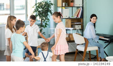 Children dancing in circle while teacher plays music on synthesizer Children dancing in circle while teacher plays music on synthesizer 141194149