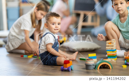 Boy playing in living room of kindergarten, group of children in background Boy playing in living room of kindergarten, group of children in background 141194202