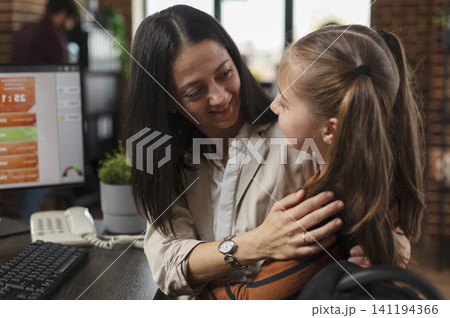 Mother hugs her little daughter at the workplace after school, mixing family affection with an office setting and an important personal conversation. Mother hugs her little daughter at the workplace after school, mixing family affection with an office setting and an important personal conversation. 141194366