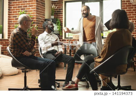 Young man addressing support group participants while participants discuss personal problems with a therapist in a supportive recovery setting. Young man addressing support group participants while participants discuss personal problems with a therapist in a supportive recovery setting. 141194373