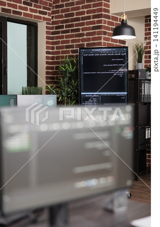 Empty data center office contains multiple computer screens showing programming code, server equipment and modern brick wall technology workspace. 141194449