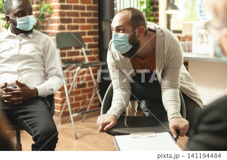 Masked man expresses anger and despair about alcohol addiction during a group therapy session, showing recovery support and emotional crisis as part of a natural therapy recovery moment involving. Masked man expresses anger and despair about alcohol addiction during a group therapy session, showing recovery support and emotional crisis as part of a natural therapy recovery moment involving. 141194484