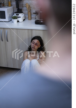 Terrified wife sits on the kitchen floor with facial bruises after abuse, showing physical trauma, fear and social problems inside a violent relationship. Terrified wife sits on the kitchen floor with facial bruises after abuse, showing physical trauma, fear and social problems inside a violent relationship. 141194612