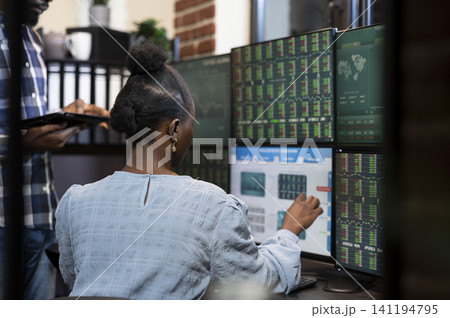 Female stock exchange advisor pointing at computer screen as she explains live updates on investments with her colleague, with black woman seated at desk with multi monitors, analyzing the forex. Female stock exchange advisor pointing at computer screen as she explains live updates on investments with her colleague, with black woman seated at desk with multi monitors, analyzing the forex. 141194795