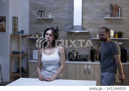 Scared woman sits in a kitchen with a drunk husband, showing alcohol abuse, relationship conflict and domestic violence in a tense home situation. Scared woman sits in a kitchen with a drunk husband, showing alcohol abuse, relationship conflict and domestic violence in a tense home situation. 141194859