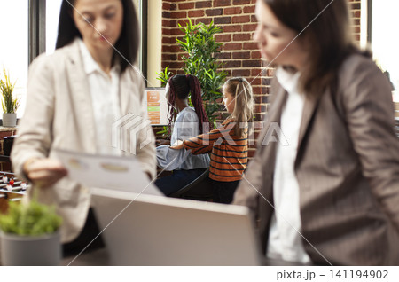 Bored girl interrupts african american employee trying to work on computer at startup office, colleagues review documents as child distracts black woman researching financial charts on desktop comput. Bored girl interrupts african american employee trying to work on computer at startup office, colleagues review documents as child distracts black woman researching financial charts on desktop comput. 141194902