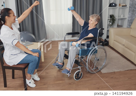 Invalid grandmother in a wheelchair performs recovery therapy with a doctor, receiving professional help for rehabilitation treatment, in a focused healthcare situation. 141194926