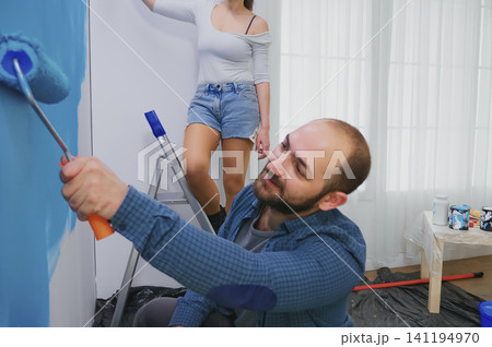 Wife paints apartment wall from ladder as a wife paints a wall from a ladder during home repair, apartment makeover and redecorating work. Wife paints apartment wall from ladder as a wife paints a wall from a ladder during home repair, apartment makeover and redecorating work. 141194970