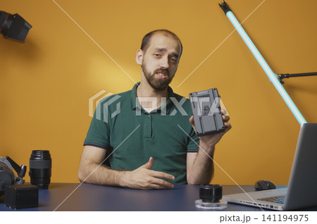 Content creator holds a V-mount battery while recording a studio review about professional camera power gear and online video workflow. Content creator holds a V-mount battery while recording a studio review about professional camera power gear and online video workflow. 141194975