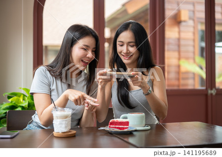 Asian women friends looking at smartphone together while enjoying coffee and dessert in a cozy cafe. Asian women friends looking at smartphone together while enjoying coffee and dessert in a cozy cafe. 141195689