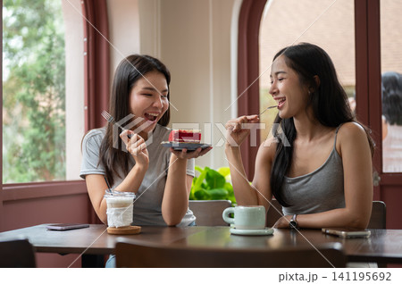 Asian women friend laughing together while enjoying coffee and red velvet cake at table in cozy cafe Asian women friend laughing together while enjoying coffee and red velvet cake at table in cozy cafe 141195692