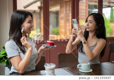 Young Asian woman photographing friend with cake in cozy cafe 141195697