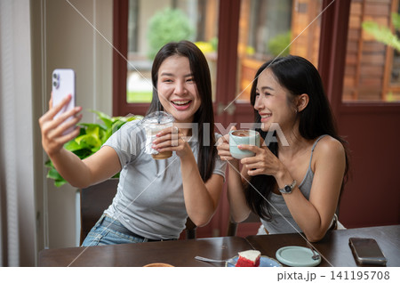 Asian female friends enjoying coffee and taking selfie in modern cafe Asian female friends enjoying coffee and taking selfie in modern cafe 141195708