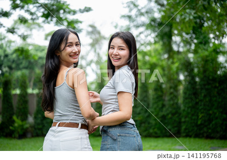 Portrait of two beautiful Asian women turning back to smile and laugh at the camera in a green garden. 141195768