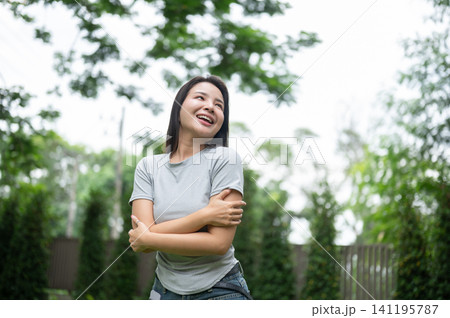 Beautiful Asian woman hugging herself and laughing happily in a backyard park. Beautiful Asian woman hugging herself and laughing happily in a backyard park. 141195787
