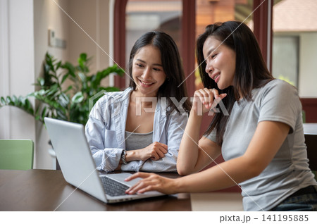 Smiling Asian woman typing on laptop while working with her teammate in cafe. Smiling Asian woman typing on laptop while working with her teammate in cafe. 141195885