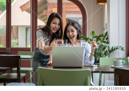 Two happy Asian women pointing at laptop screen during teamwork Two happy Asian women pointing at laptop screen during teamwork 141195910