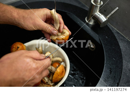 Water runs from a faucet as a person washes mushrooms in a bowl.  141197274