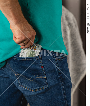 Man places cash in back pocket of jeans while standing in casual setting Man places cash in back pocket of jeans while standing in casual setting 141197534