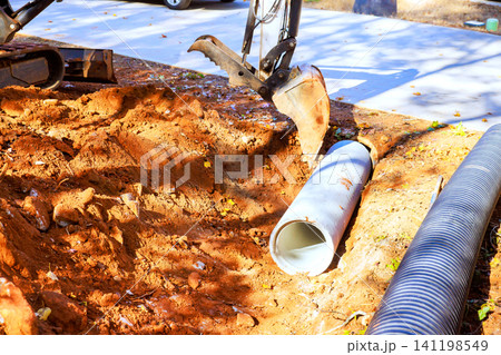 Construction workers dig trench, place cement pipe inground Construction workers dig trench, place cement pipe inground 141198549