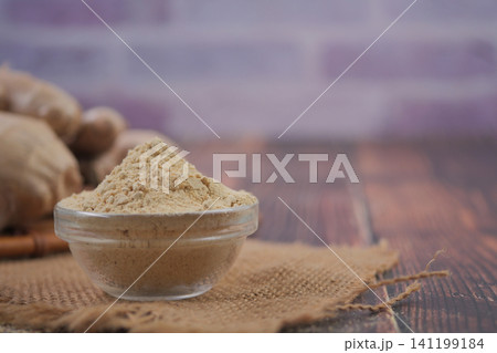 Ginger powder on a wooden table with fresh ginger nearby 141199184