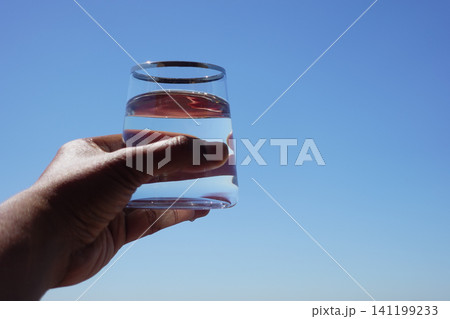 Holding a glass of water under a clear blue sky Holding a glass of water under a clear blue sky 141199233