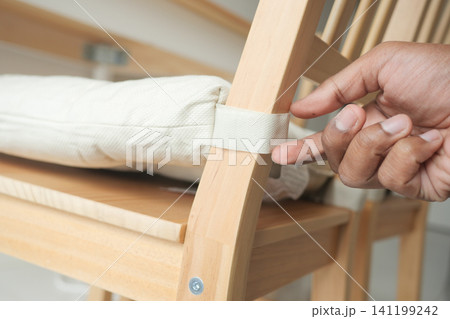 Hand adjusting cushion on wooden chair in a bright room Hand adjusting cushion on wooden chair in a bright room 141199242