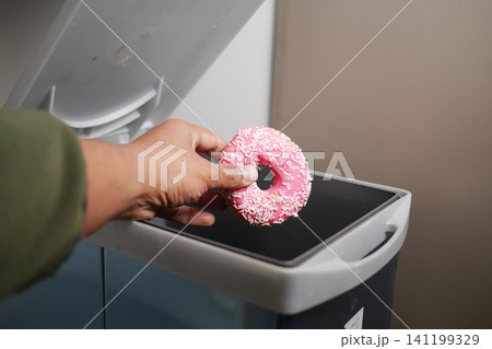 Hand holding a pink donut over a trash bin 141199329