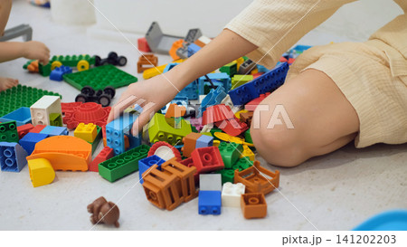 Children sitting on the floor sorting and arranging colorful plastic construction blocks scattered around them. Educational play concept Children sitting on the floor sorting and arranging colorful plastic construction blocks scattered around them. Educational play concept 141202203