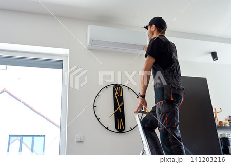 Air conditioner technician inspecting wall mounted AC unit in home 141203216