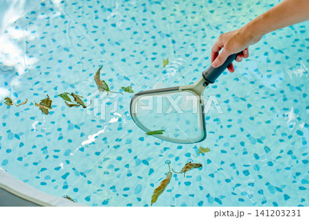Hand removing fallen leaves from hot tub water with pool skimmer Hand removing fallen leaves from hot tub water with pool skimmer 141203231
