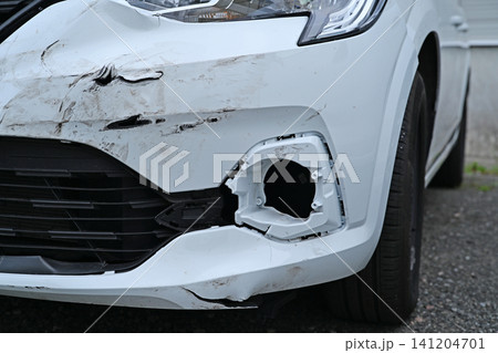 Damaged front bumper of a white car after a traffic accident, close-up view with scratches. Damaged front bumper of a white car after a traffic accident, close-up view with scratches. 141204701