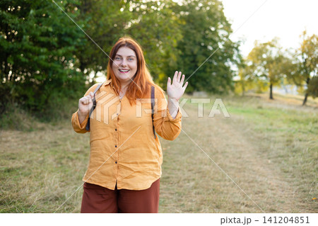Smiling Red Haired Woman Backpacker Waving Hand in Green Forest 141204851