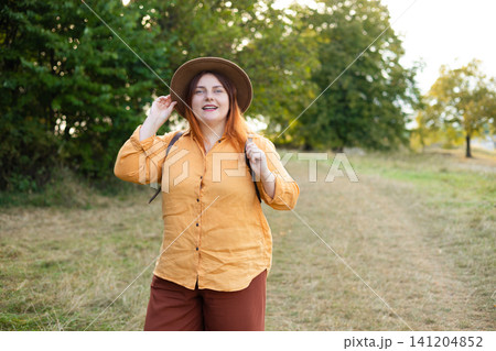 Happy Woman Backpacker in Hat and Orange Shirt Hiking in Green Forest Happy Woman Backpacker in Hat and Orange Shirt Hiking in Green Forest 141204852