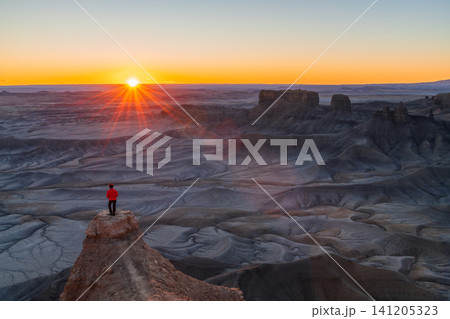Majestic sunrise over vast desert landscape brings feelings of awe and wonder as lone person standing on high rock formation looks out over beautiful badlands of utah usa Majestic sunrise over vast desert landscape brings feelings of awe and wonder as lone person standing on high rock formation looks out over beautiful badlands of utah usa 141205323