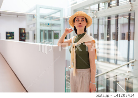 Mid shot of young Caucasian elegant woman in suit and straw hat posing in the modern art gallery. Concept of cultural education and Museum day Mid shot of young Caucasian elegant woman in suit and straw hat posing in the modern art gallery. Concept of cultural education and Museum day 141205414