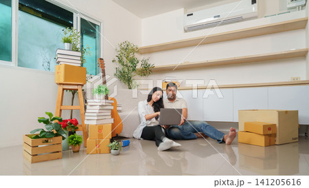 South Asian couple using laptop together while unpacking in new apartment 141205616