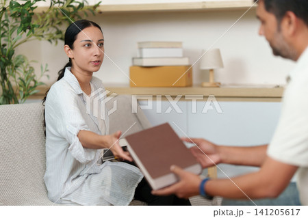 South Asian woman passing book to man while unpacking in new home South Asian woman passing book to man while unpacking in new home 141205617