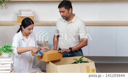 South Asian woman sealing cardboard box with tape dispenser for moving house 141205644