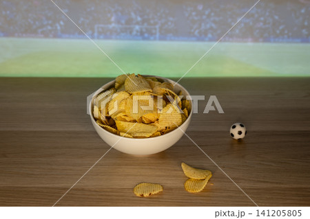 Bowl of potato chips on a table with a small soccer ball decoration, creating a football night atmosphere with comforting food. Bowl of potato chips on a table with a small soccer ball decoration, creating a football night atmosphere with comforting food. 141205805