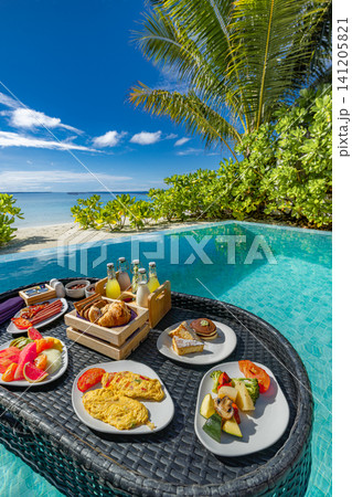 Vertical shot of floating breakfast in plunge pool under palm fronds. Gourmet morning spread with fruit and dishes on woven tray, tropical villa setting. Stylish resort indulgence scene for social Vertical shot of floating breakfast in plunge pool under palm fronds. Gourmet morning spread with fruit and dishes on woven tray, tropical villa setting. Stylish resort indulgence scene for social 141205821