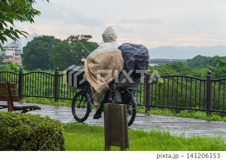 雨の日にカッパを着て自転車に乗る女性 雨の日にカッパを着て自転車に乗る女性 141206153