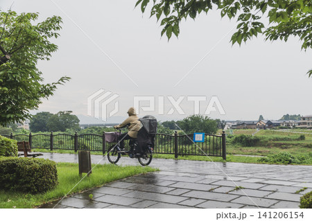 雨の日にカッパを着て自転車に乗る女性 雨の日にカッパを着て自転車に乗る女性 141206154