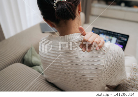 Exhausted asian woman sitting on comfortable sofa experiencing severe shoulder pain during stressful laptop work representing difficult remote office lifestyle with intense uncomfortable feeling Exhausted asian woman sitting on comfortable sofa experiencing severe shoulder pain during stressful laptop work representing difficult remote office lifestyle with intense uncomfortable feeling 141206314